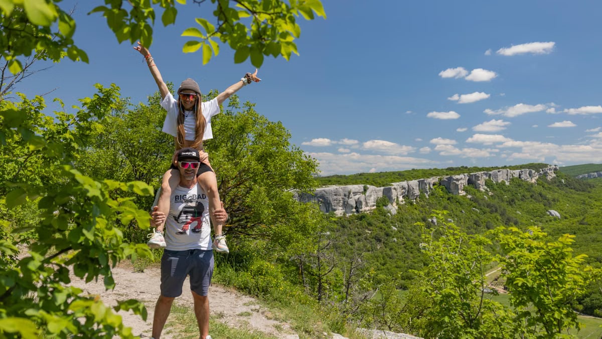 A couple enjoys a playful piggyback ride on a scenic countryside hike under a sunny sky.